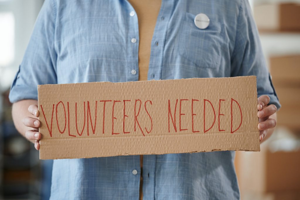 A Person Holding a Cardboard with Inscription "Volunteers needed"